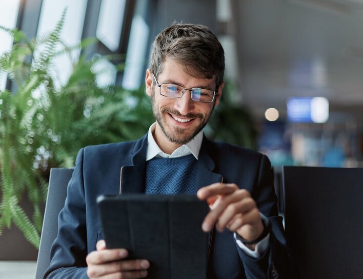Titelbild Bachelor Wirtschaftswissenschaften Ein junger Mann im Business-Outfit hält ein Tablet in der Hand und schaut lächelnd darauf.