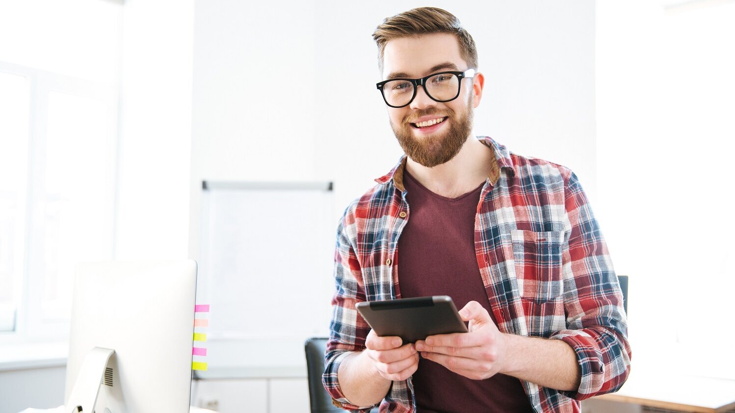 Mann steht mit Tablet in der Hand vor einem Schreibtisch